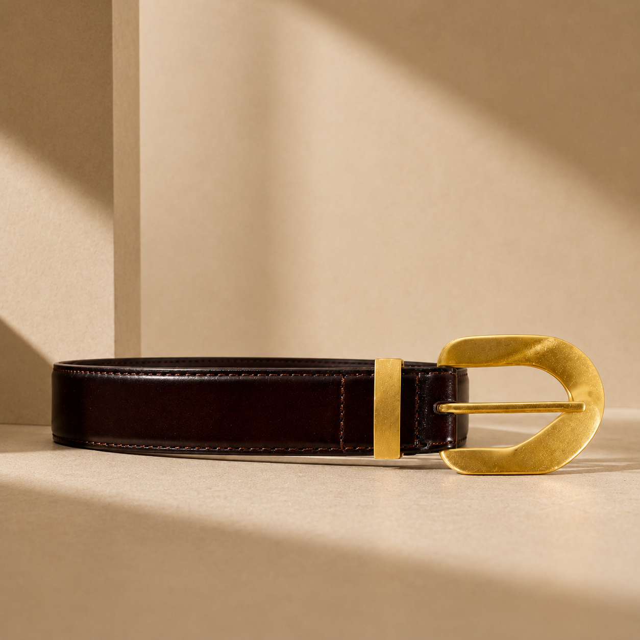 Black leather belt with a gold buckle on a beige background