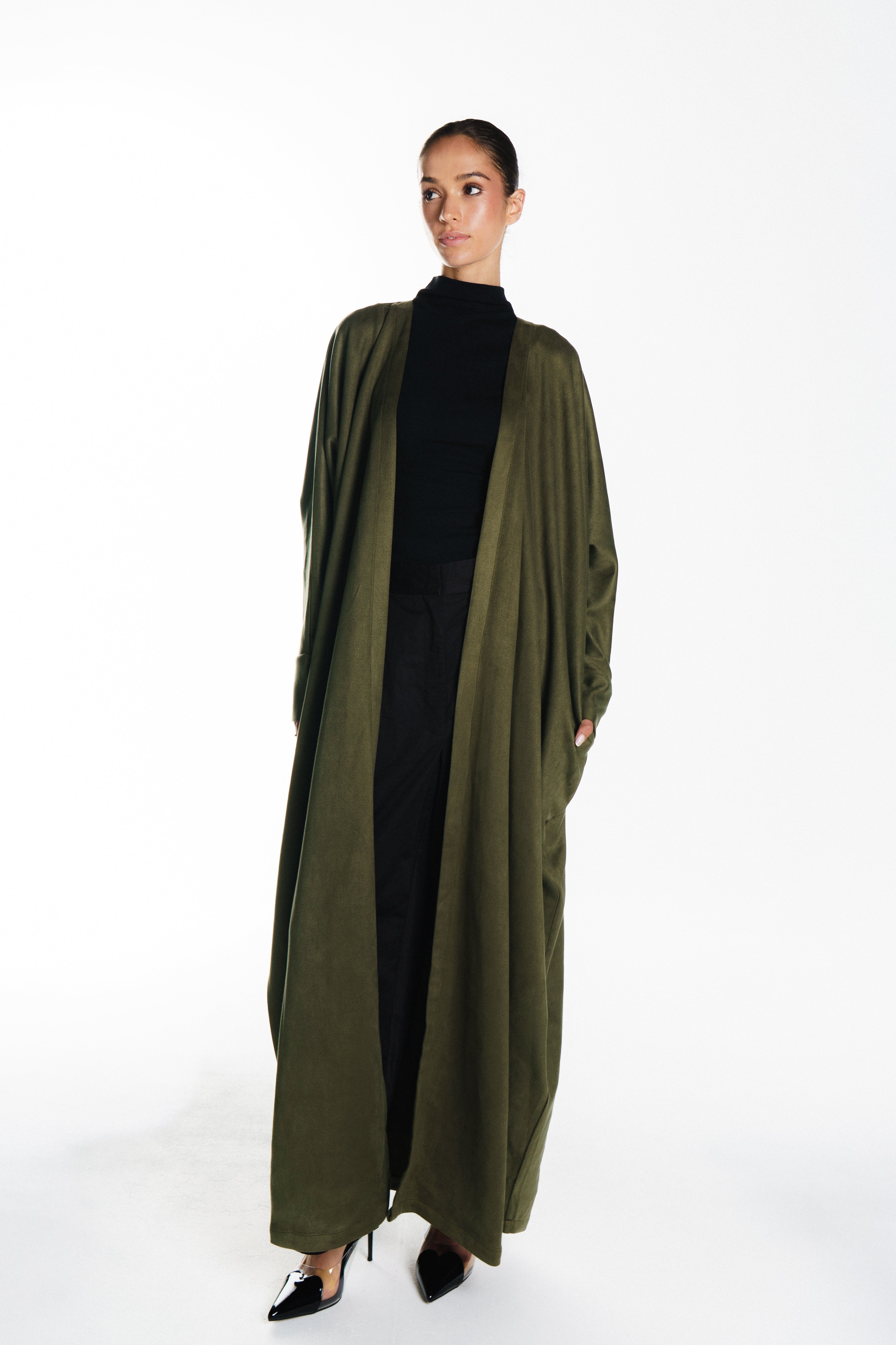 Woman wearing a long olive green coat over a black outfit on a white background